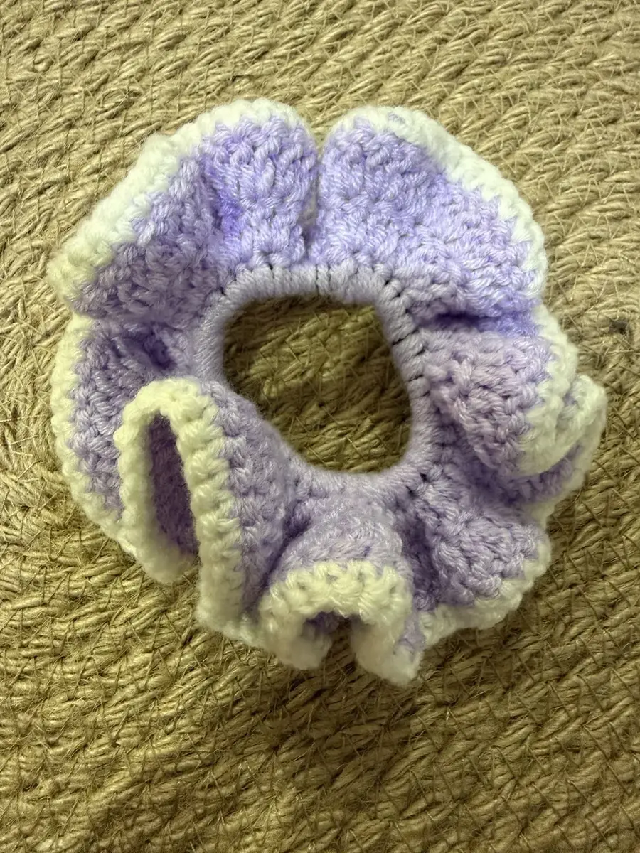 A handmade ruffle scrunchie in lilac with a pale yellow edge.