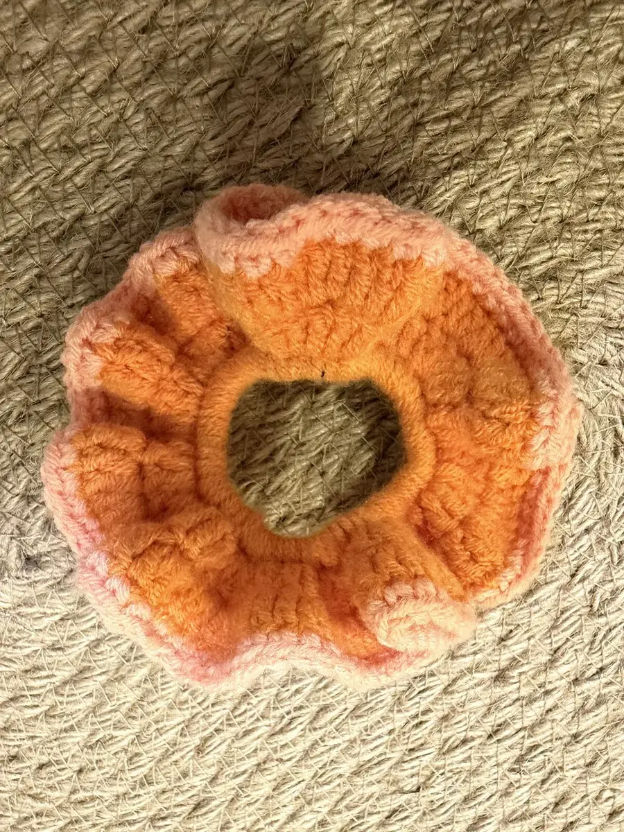 A handmade ruffle scrunchie in orange with a peach edge.