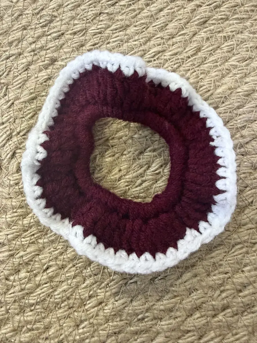 A handmade ruffle scrunchie in maroon with a white edge.