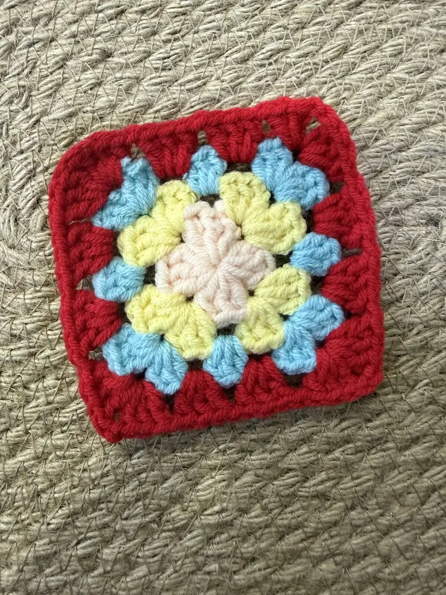 A granny square with a red border and blue, yellow and pink.