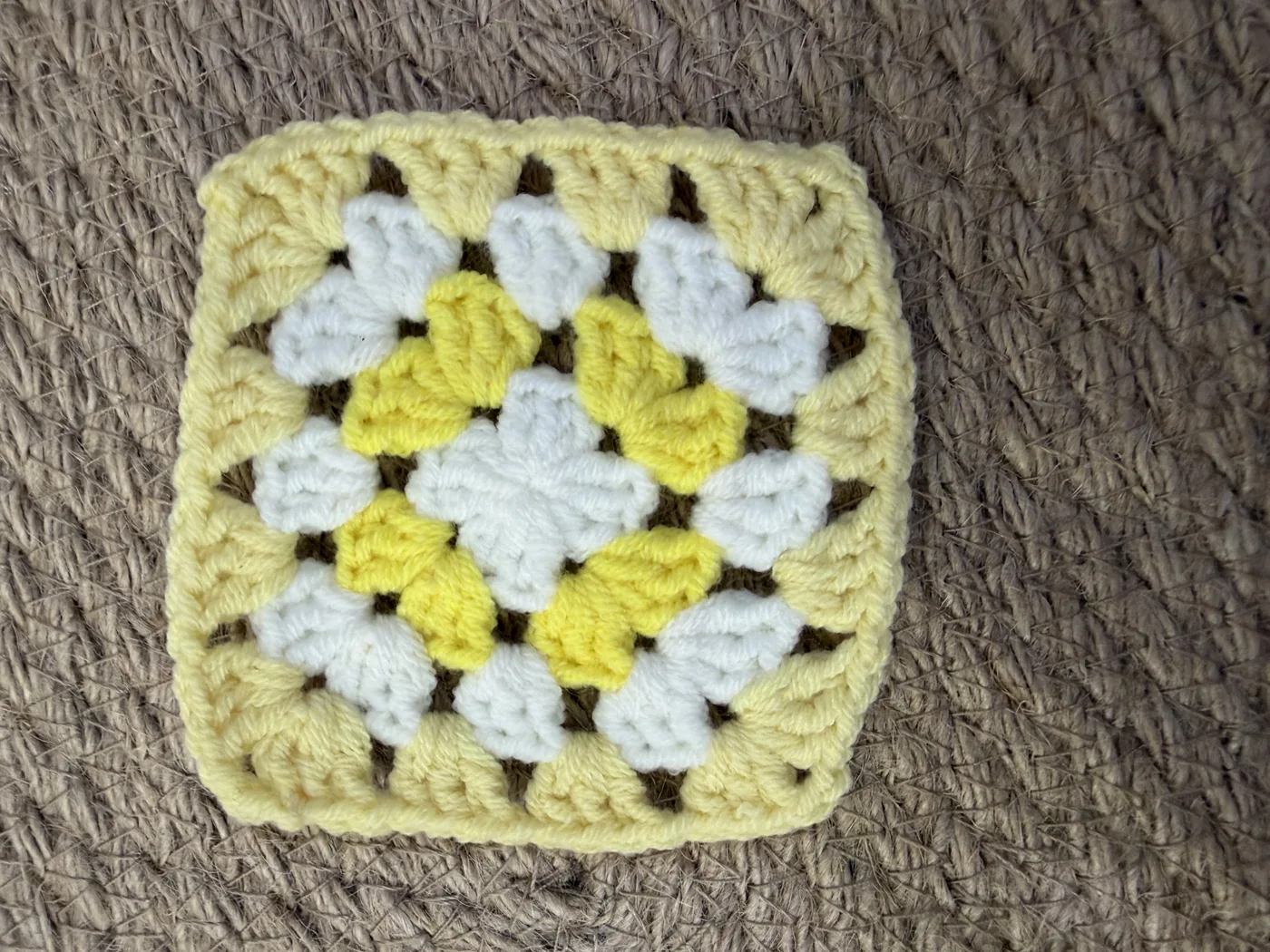 A crochet granny square in yellow and white, like a daisy.