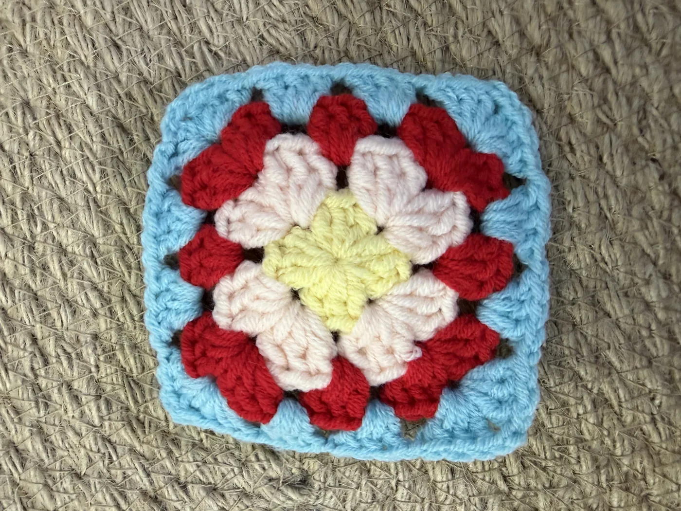 A crochet granny square in red, white and light blue.