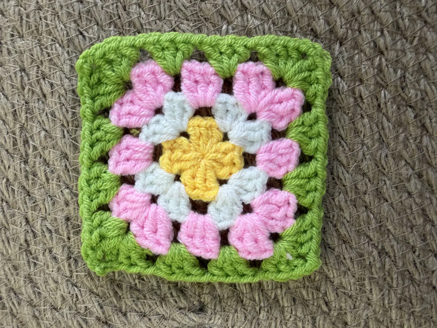 A crochet granny square in pink and yellow with a green border.
